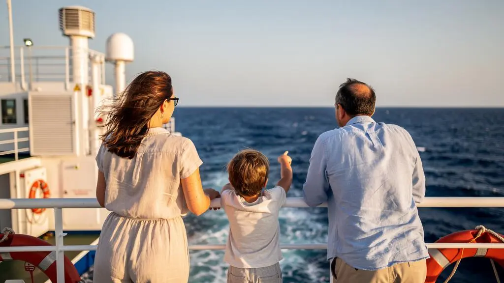 Famiglia in piedi alla ringhiera del ponte del traghetto che guarda il Mar Mediterraneo durante la traversata verso la Sardegna
